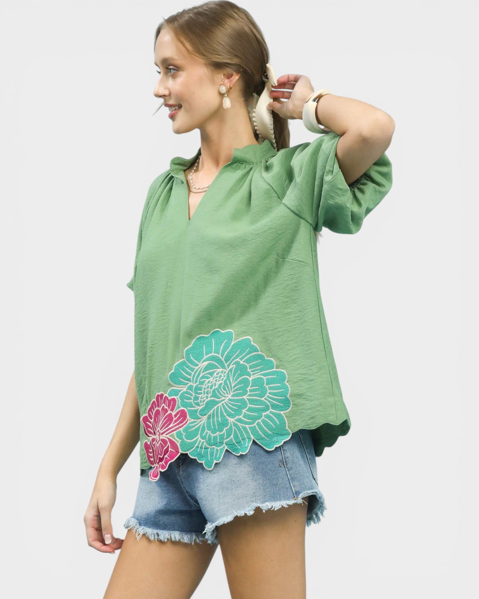 Woman wearing a green oversized shirt with floral designs on a plain background