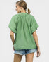 Woman wearing a green top and denim shorts on a plain background