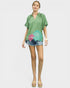 Woman wearing a green top with floral design and denim shorts on a white background