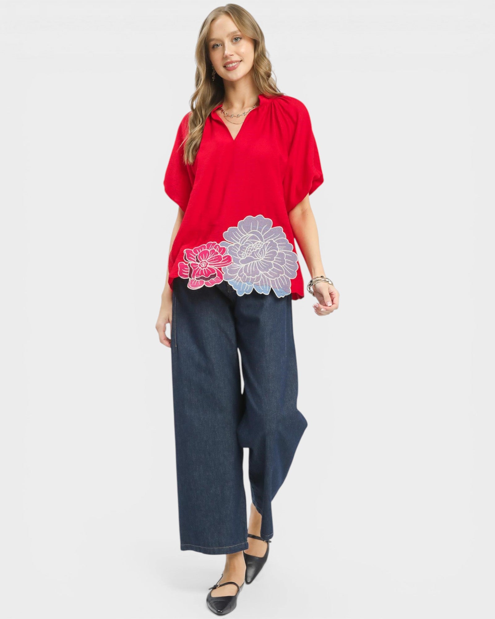 Woman wearing a red blouse with floral design and blue pants on a white background