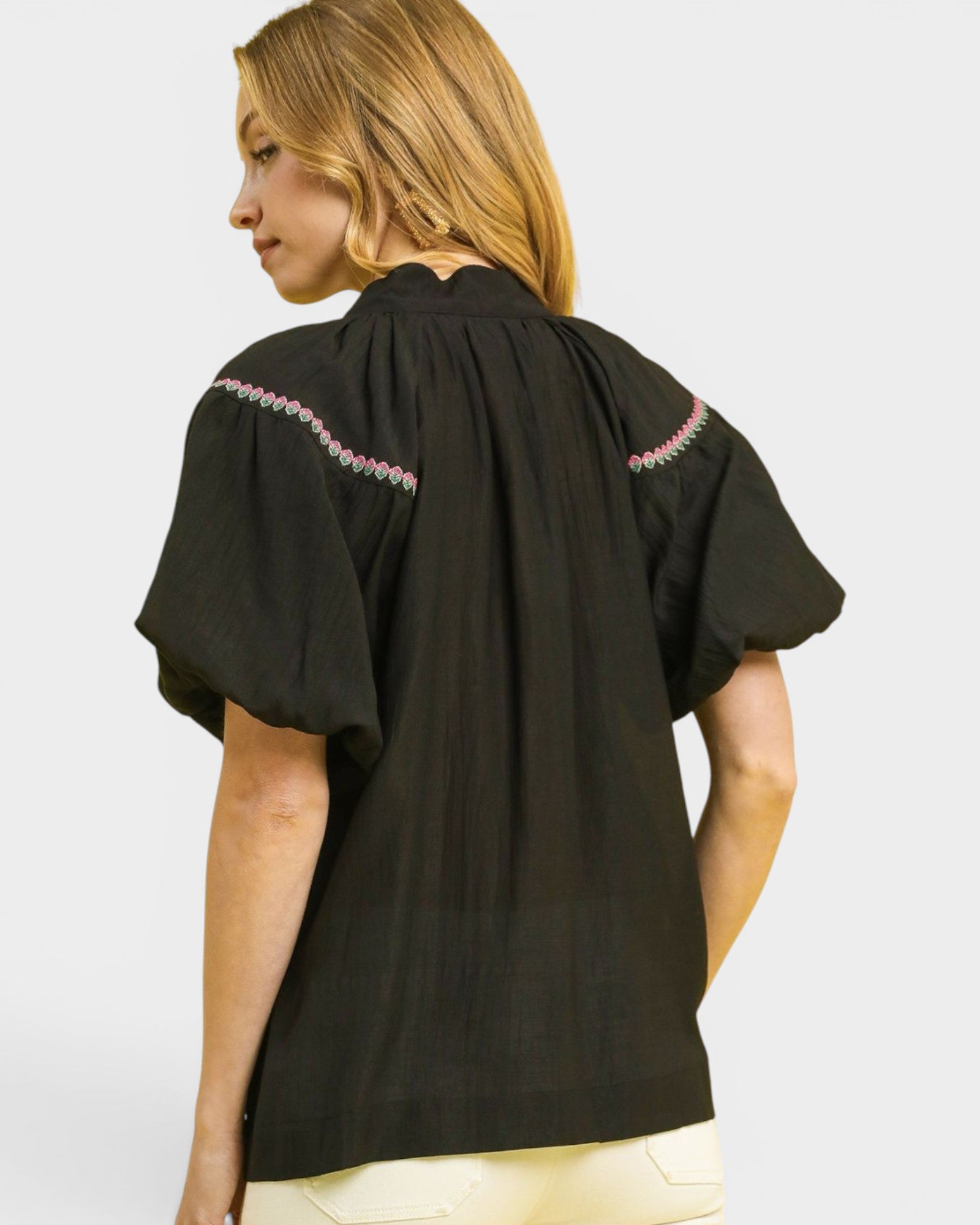 Woman wearing a black blouse with pink embroidery on a white background
