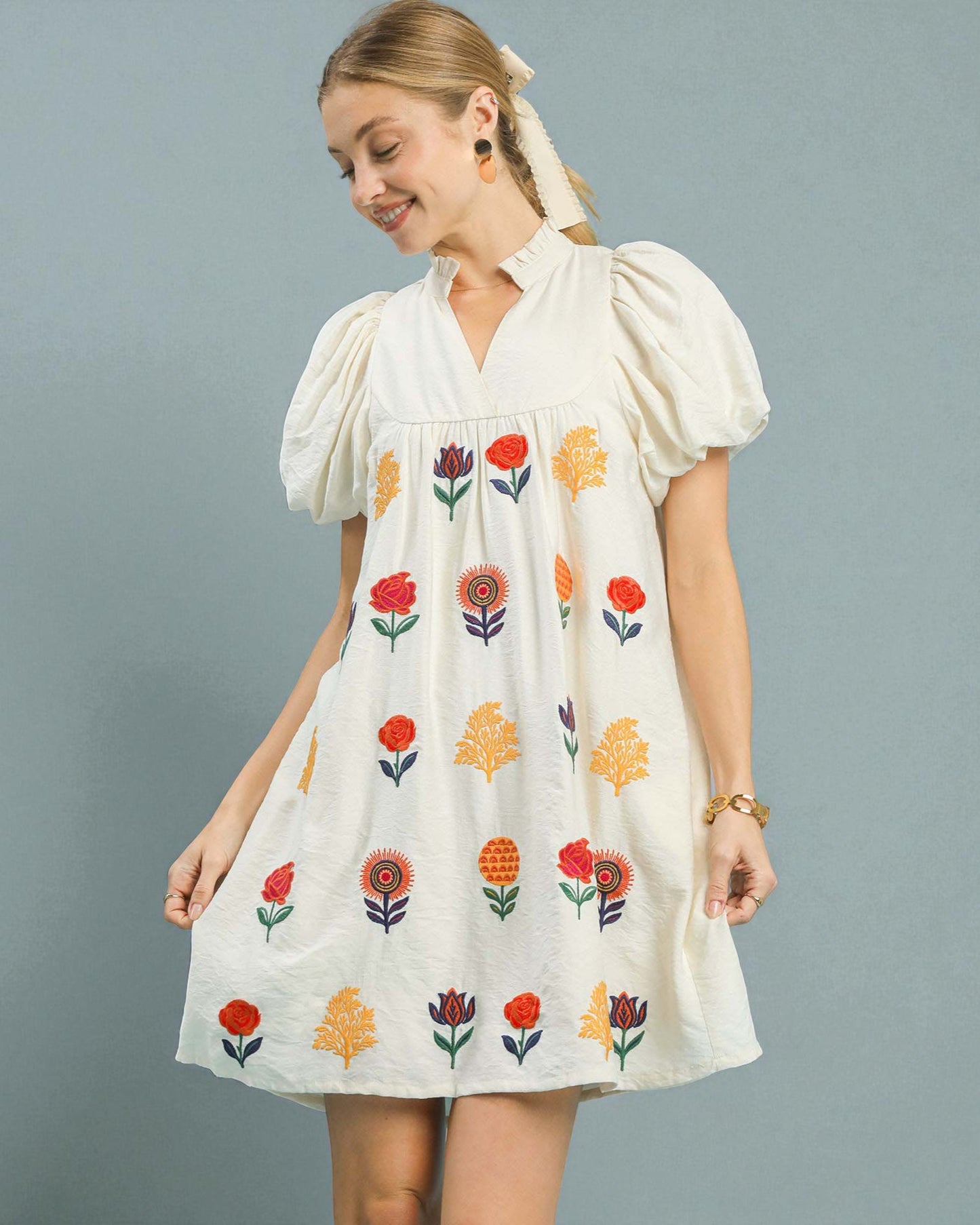 Woman wearing a white dress with floral embroidery on a gray background