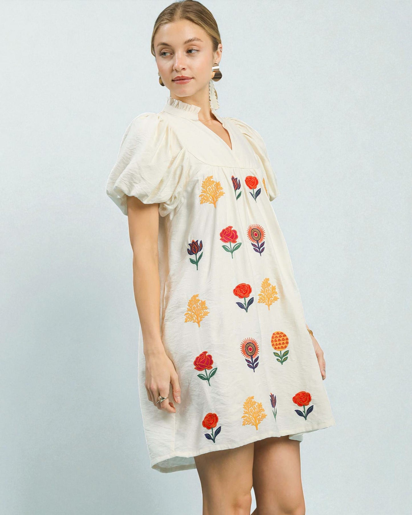 Woman wearing a white dress with colorful floral embroidery on a light gray background