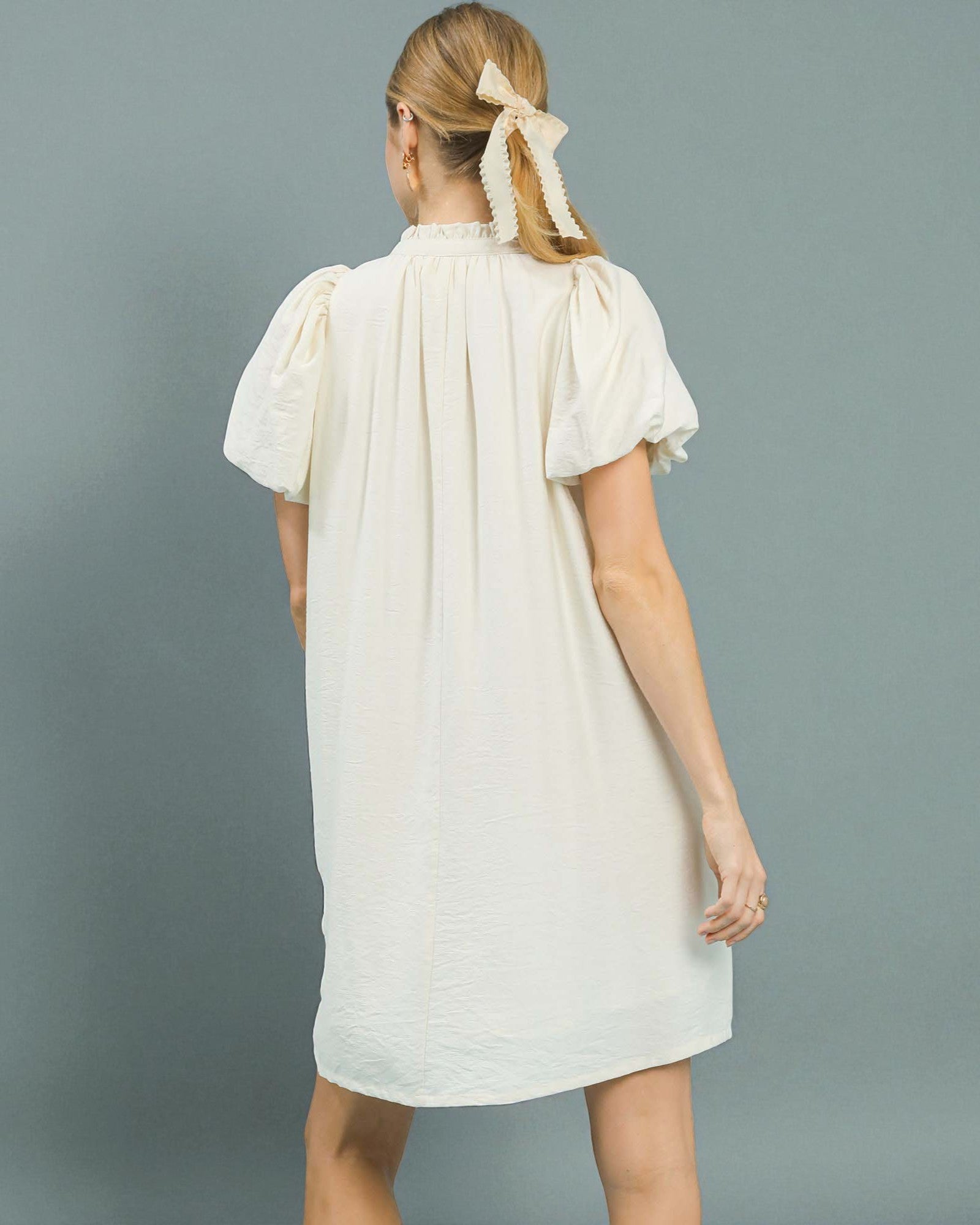 Woman wearing a white dress with puffed sleeves against a gray background