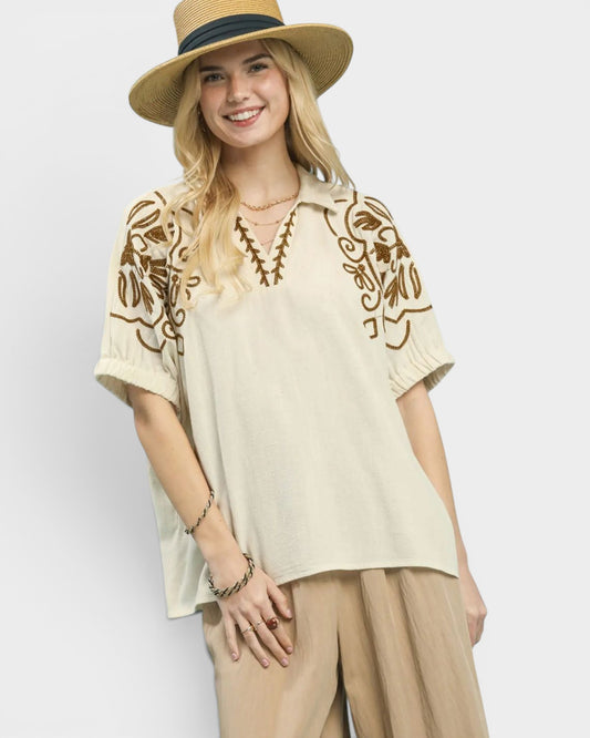 Woman wearing a beige embroidered top and hat on a white background