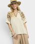 Woman wearing a beige embroidered top and hat on a white background