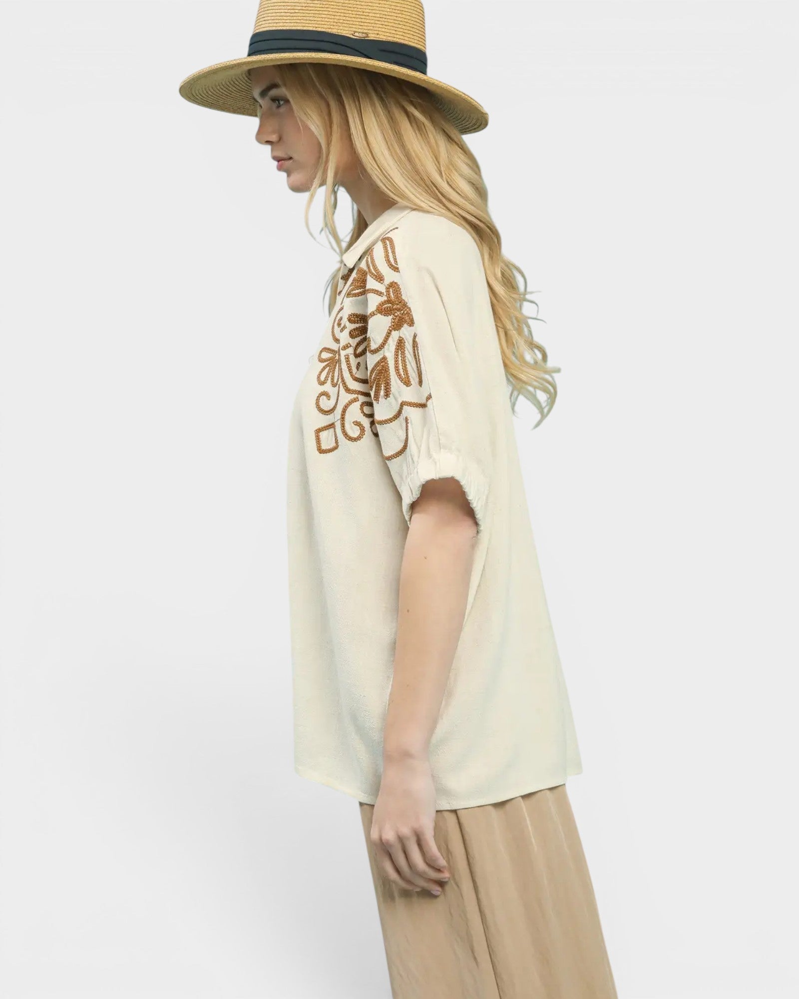 Woman wearing a beige blouse with floral embroidery and a straw hat on a white background