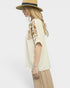 Woman wearing a beige blouse with floral embroidery and a straw hat on a white background