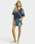 Woman wearing a navy blue embroidered top and denim shorts on a white background