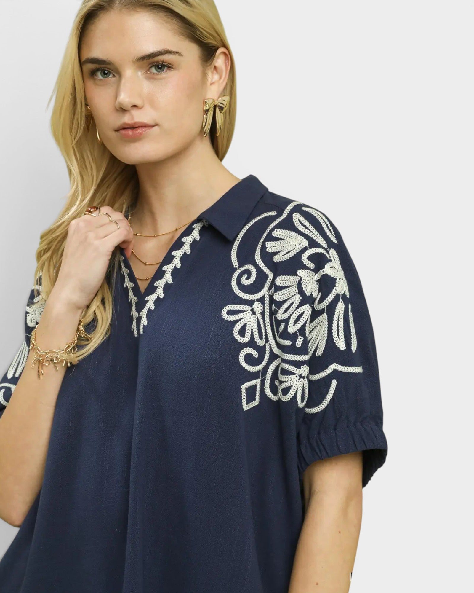 Woman wearing a navy blue top with white floral embroidery on a plain background