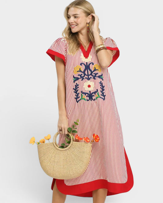 Woman wearing a red and white striped dress with colorful embroidery, holding a straw bag.