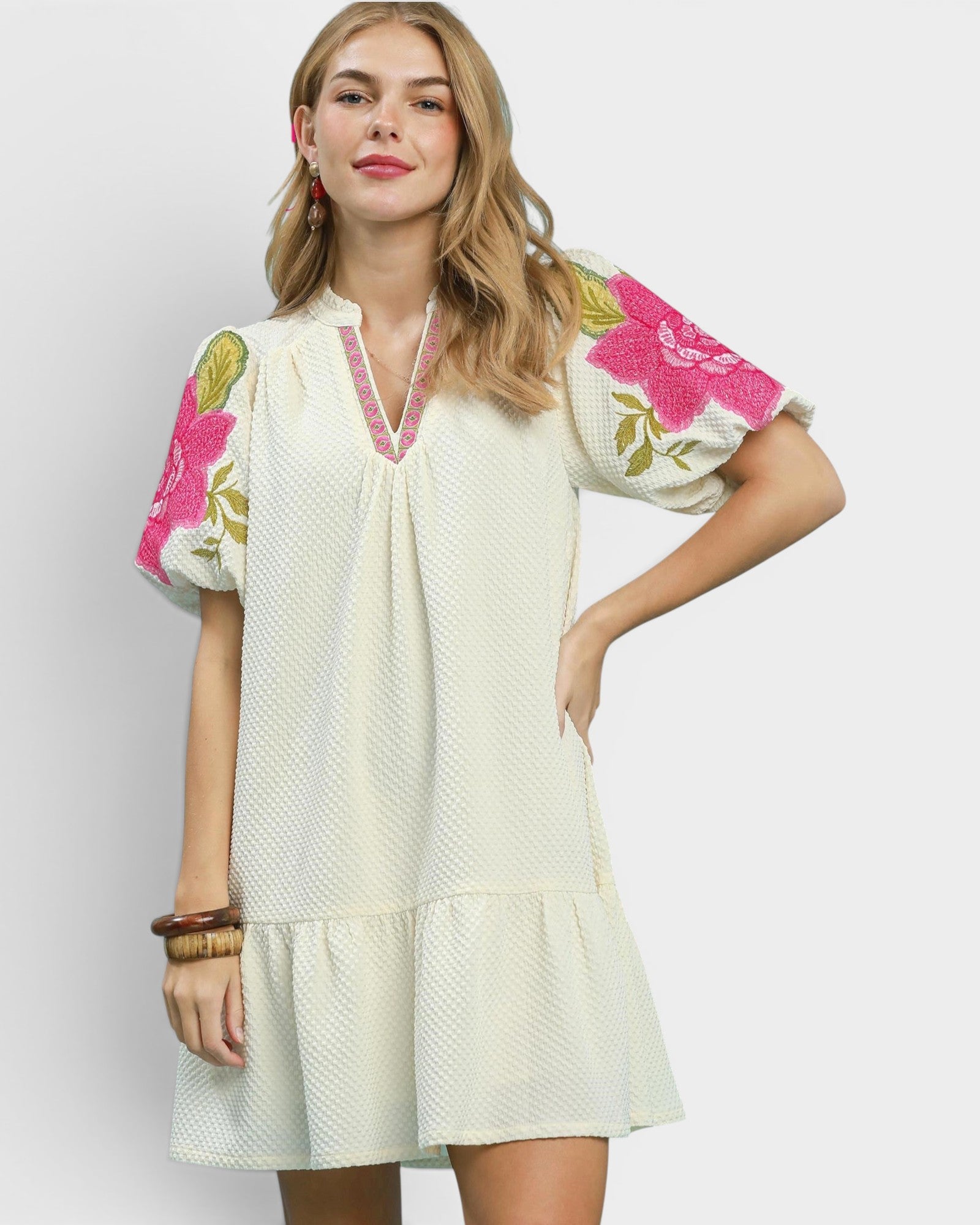 Woman wearing a white dress with floral embroidery on a plain background