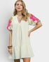 Woman wearing a white dress with floral embroidery on a plain background