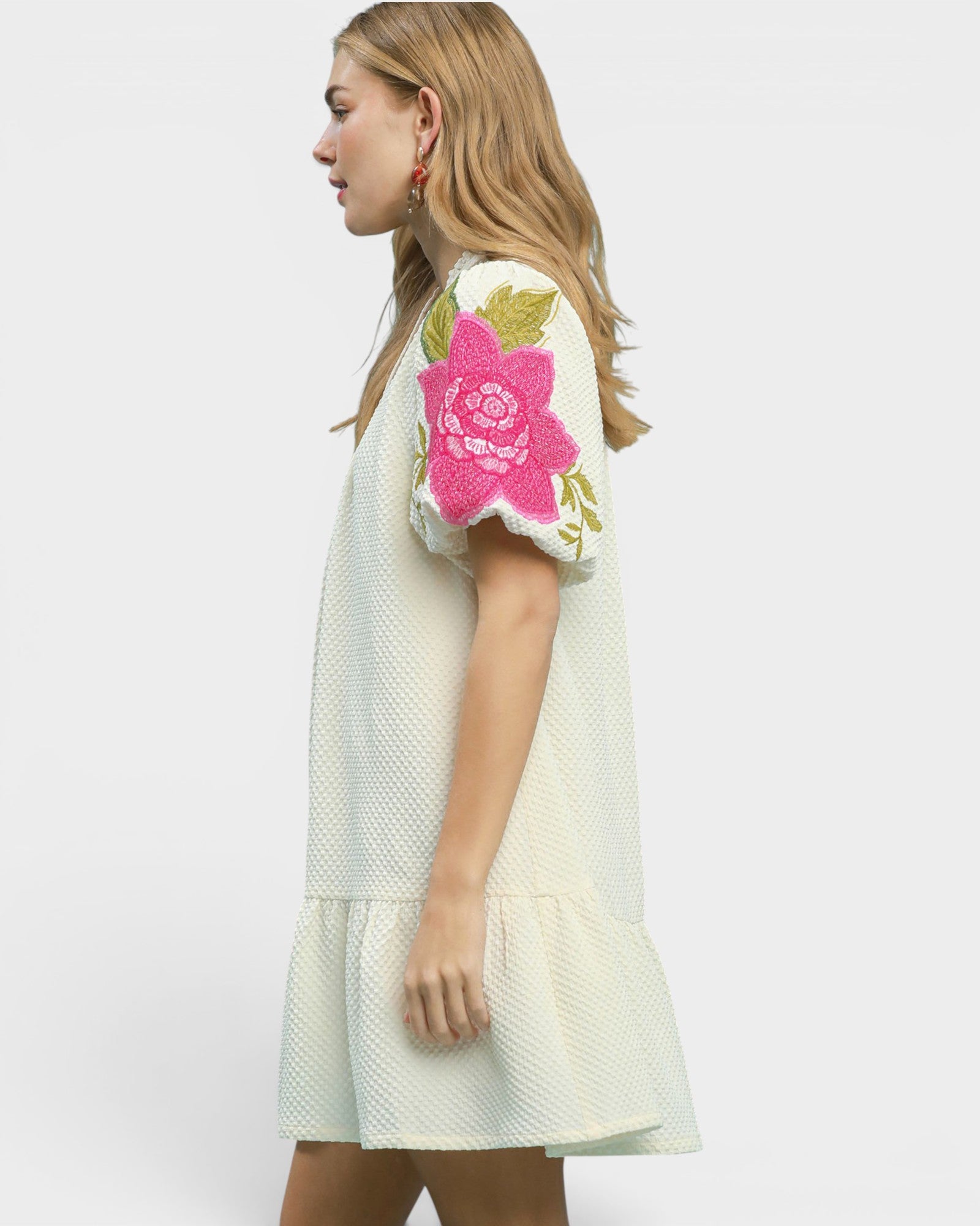 Woman wearing a white dress with floral embroidery on a plain background
