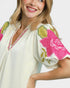 Woman wearing a white blouse with pink floral embroidery on a plain background
