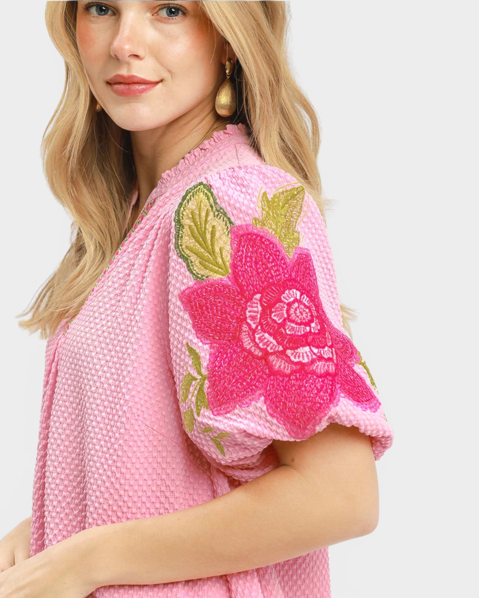 Woman wearing a pink top with floral embroidery on a white background