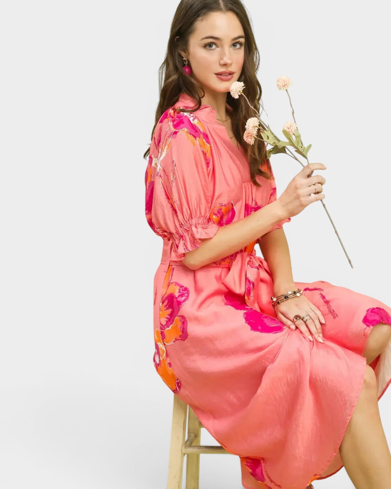 Woman in a pink floral dress holding flowers on a white background
