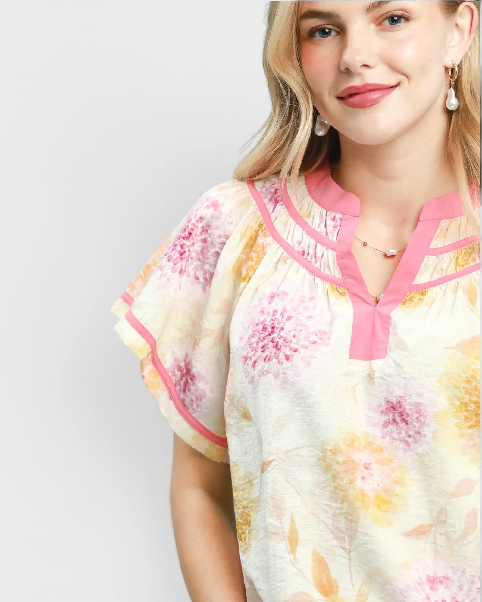 Woman wearing a floral blouse with pink accents on a plain background