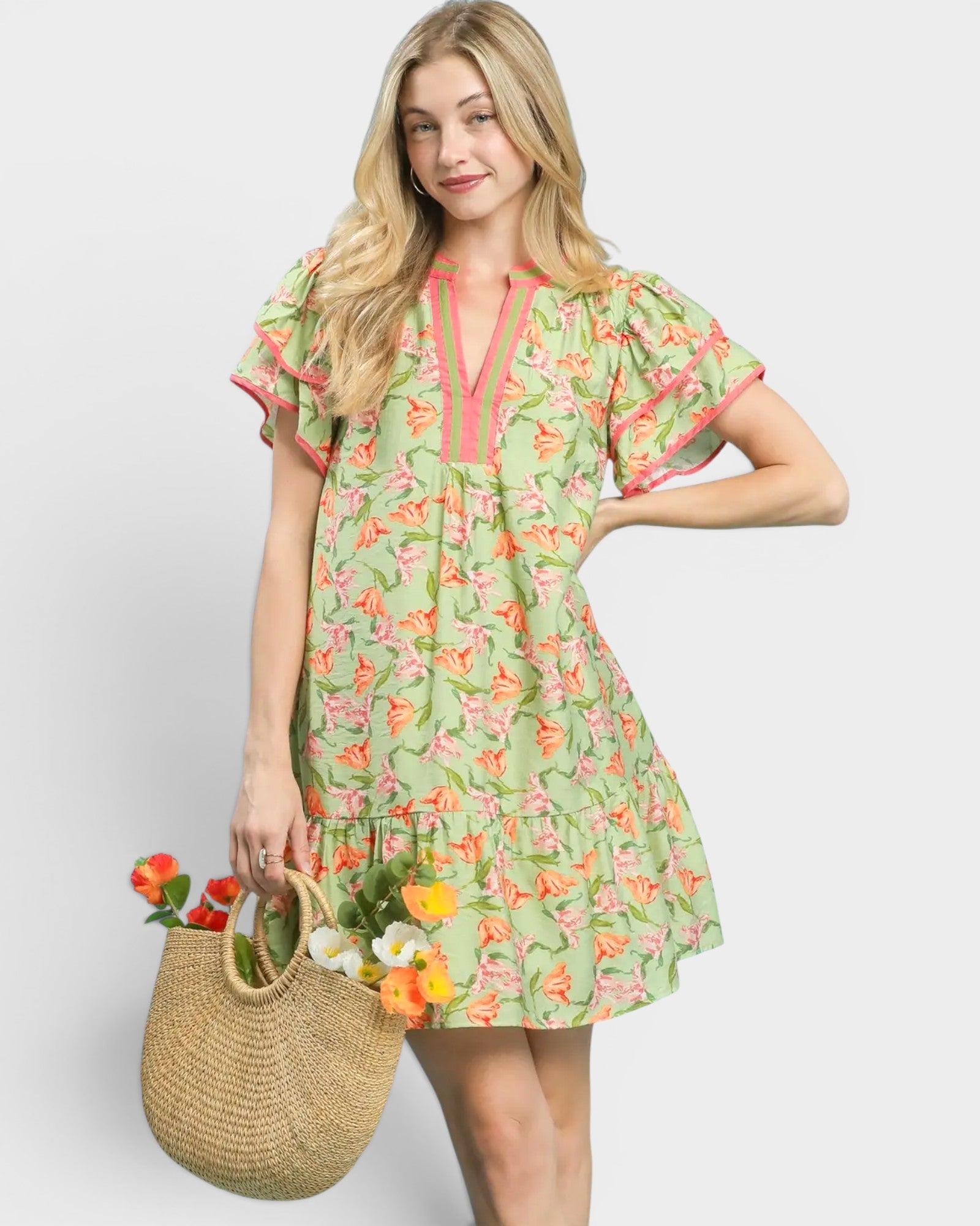 Woman wearing a green floral dress holding a straw bag with flowers on a white background