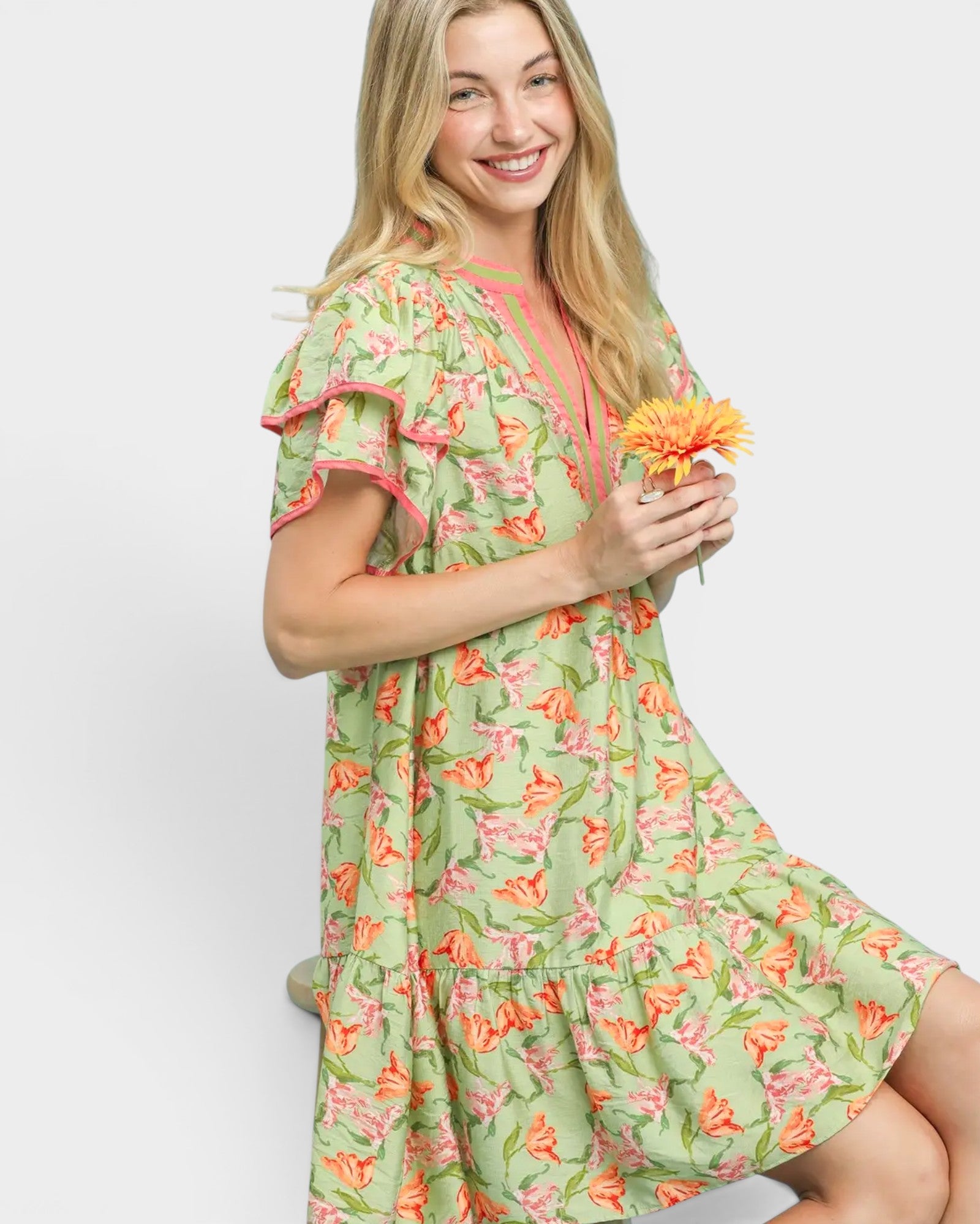 Woman wearing a green floral dress holding a flower against a white background