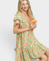 Woman wearing a green floral dress holding a flower against a white background