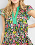 Woman wearing a colorful floral dress with green trim on a plain background