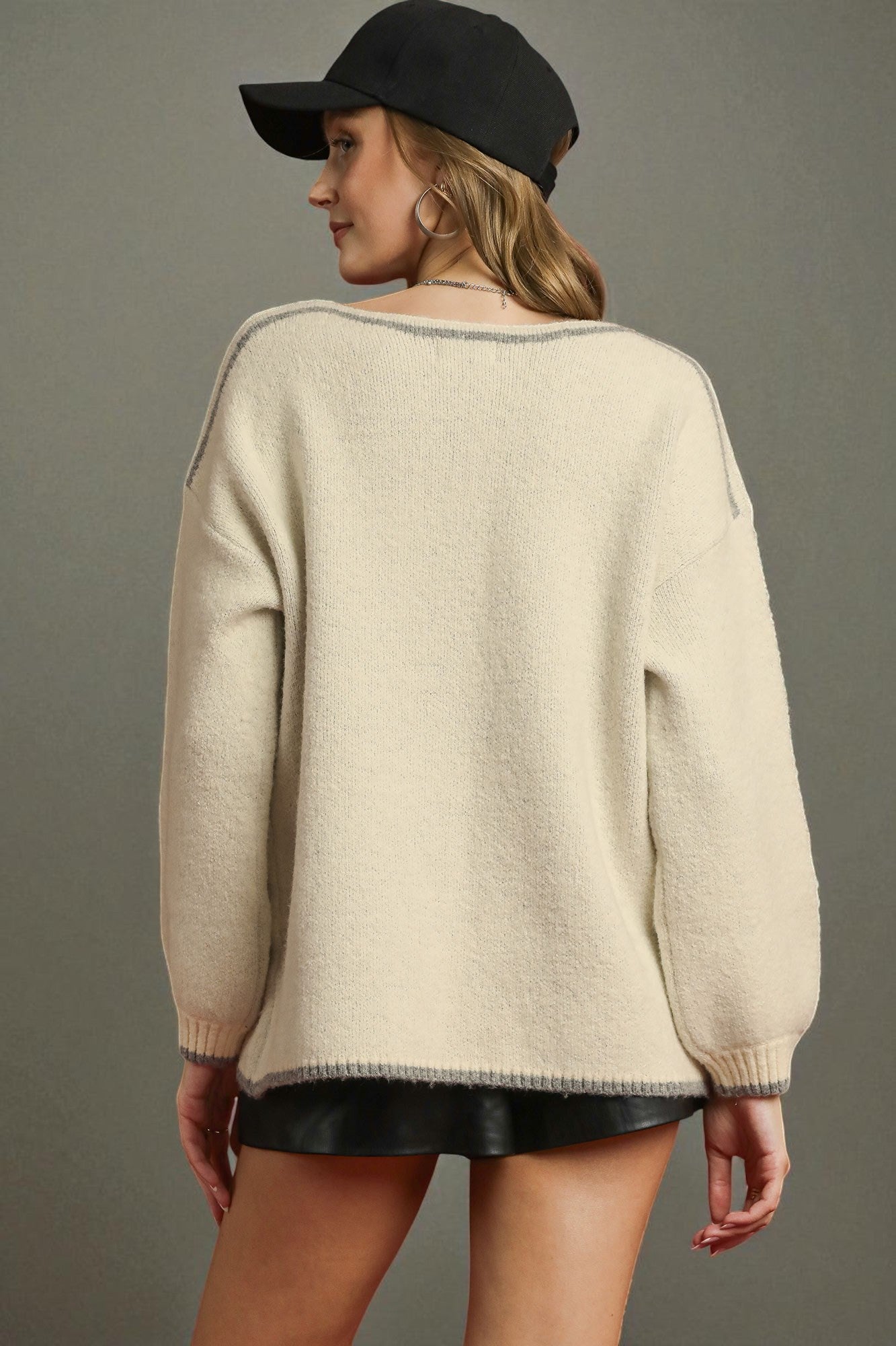 Person wearing a beige sweater and black cap on a gray background