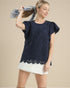 Woman wearing a navy blue lace top with white shorts on a beige background