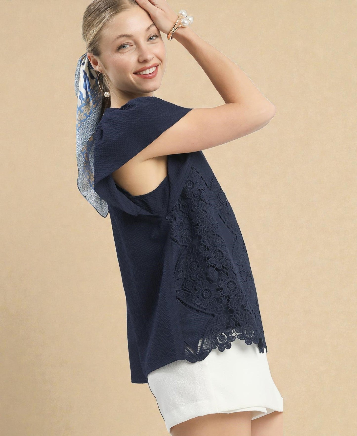 Woman wearing a navy blue lace top and white shorts on a beige background
