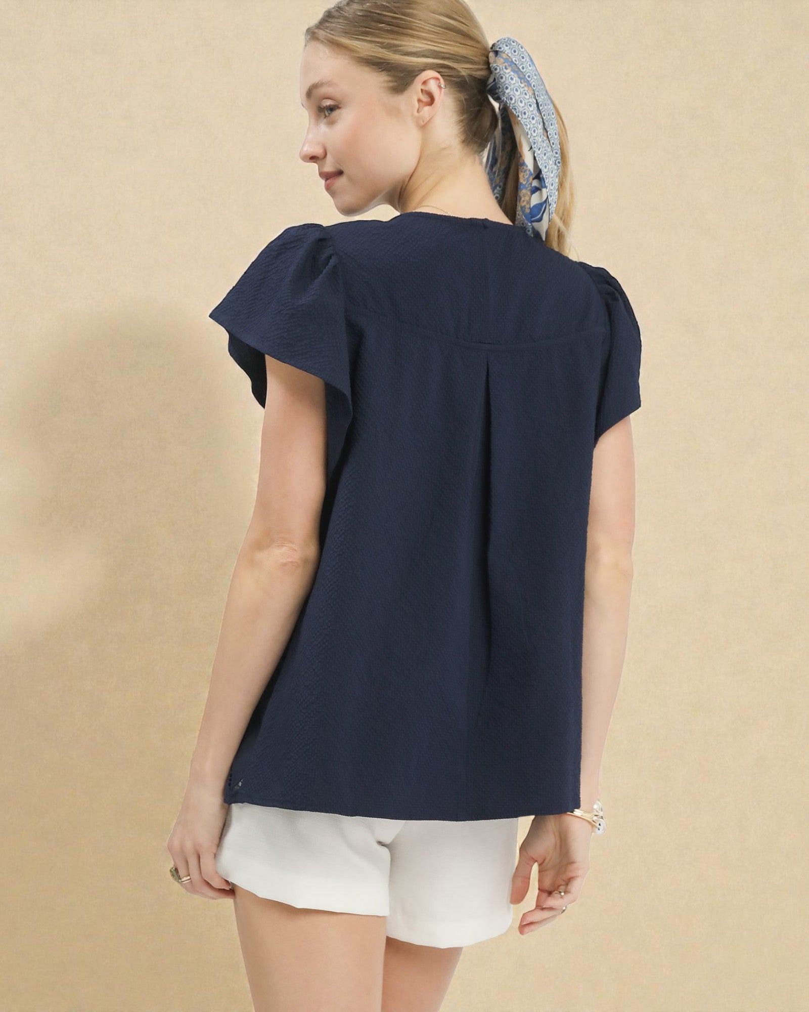 Woman wearing a navy blue blouse with ruffled sleeves on a beige background