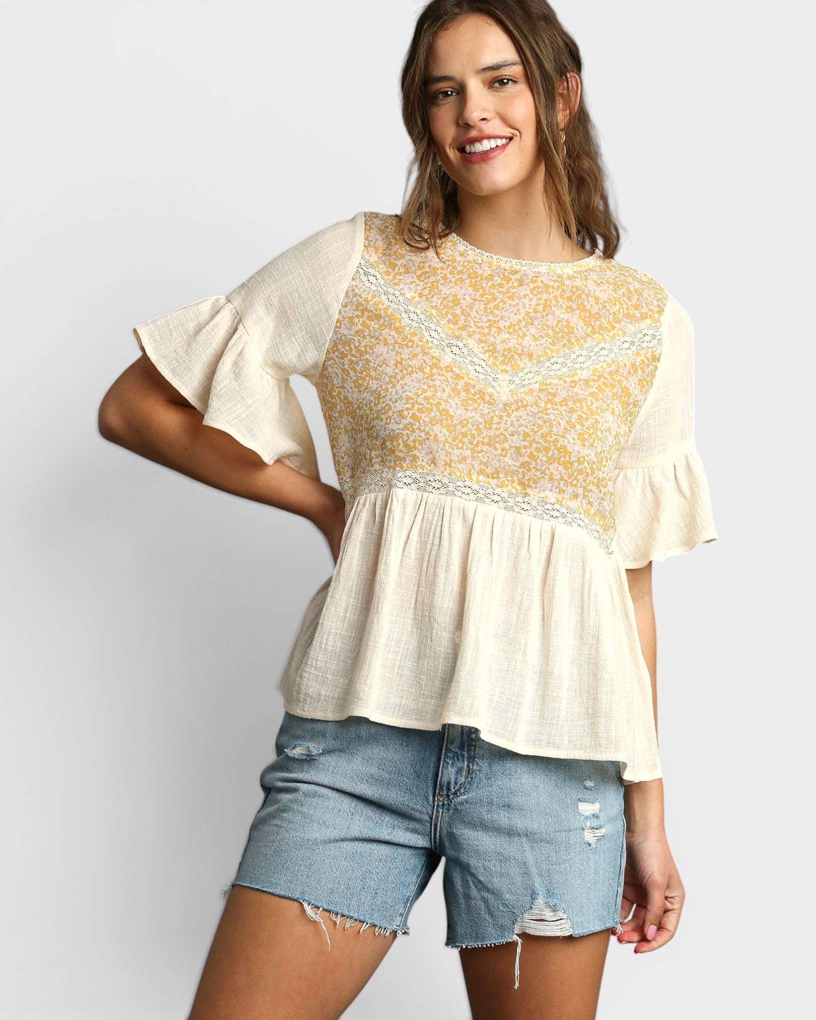 Woman wearing a yellow and white blouse with denim shorts on a plain background
