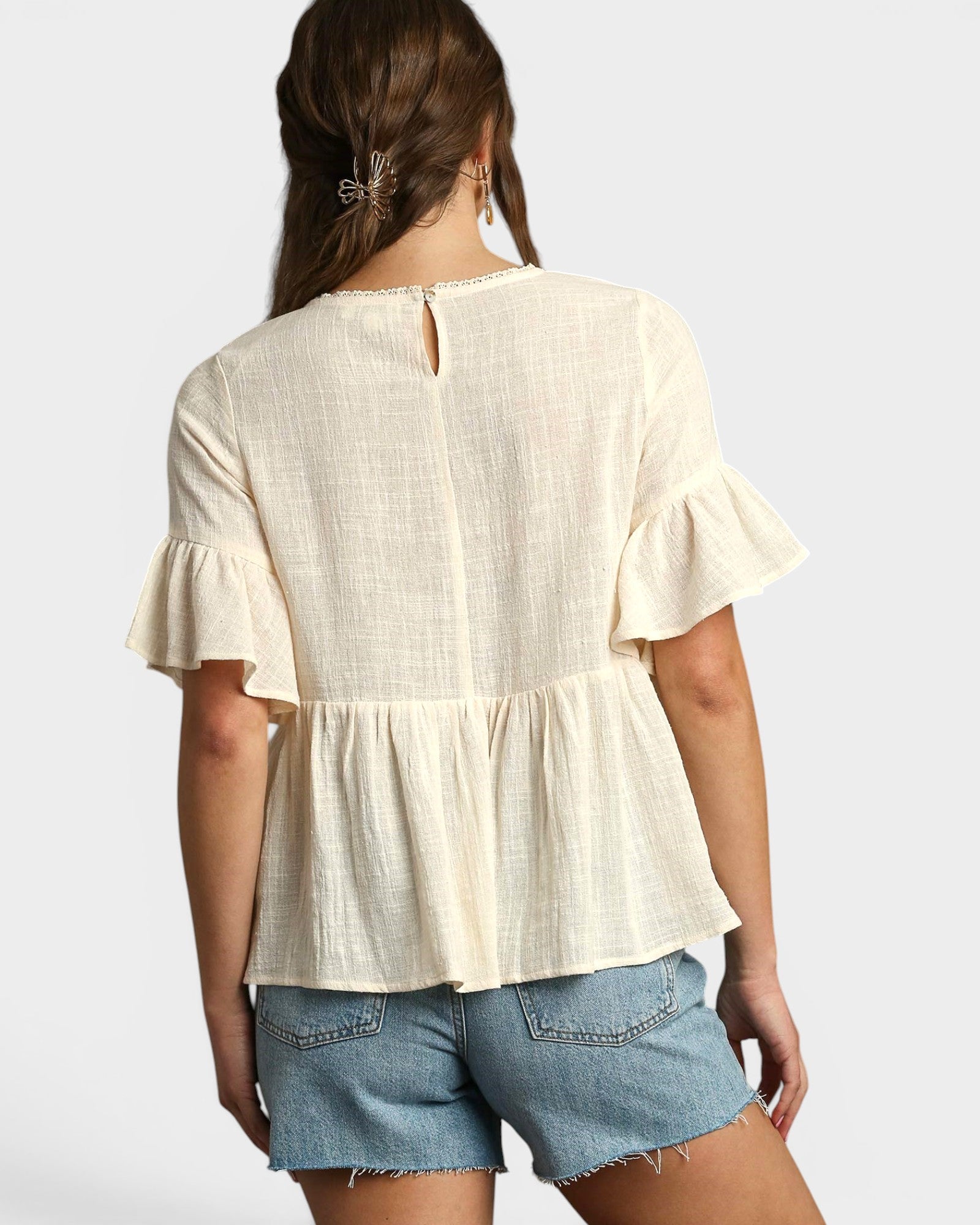 Woman wearing a cream peplum top and denim shorts on a white background