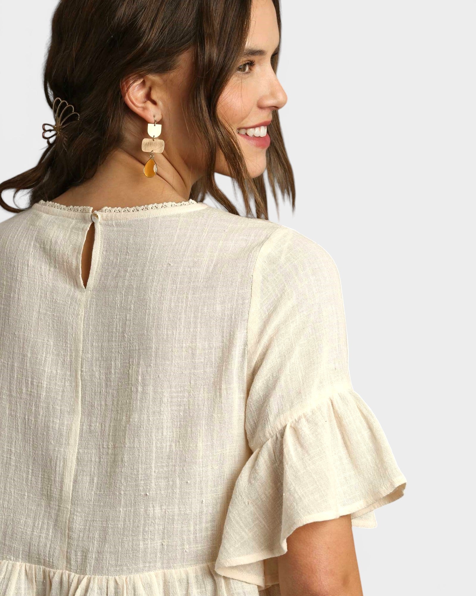 Woman wearing a beige dress with ruffled sleeves on a plain background