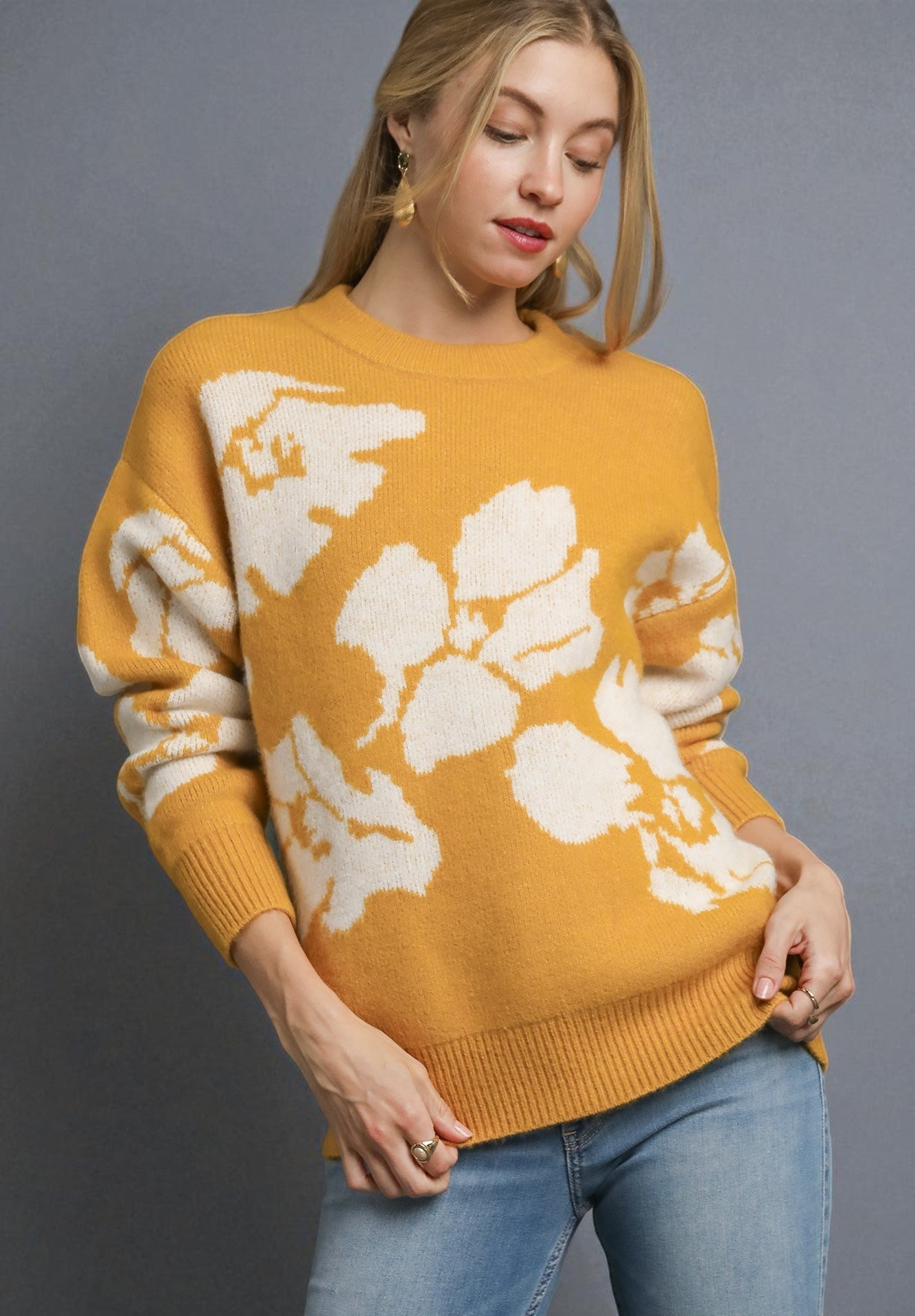 Woman wearing a mustard yellow sweater with white floral patterns on a gray background