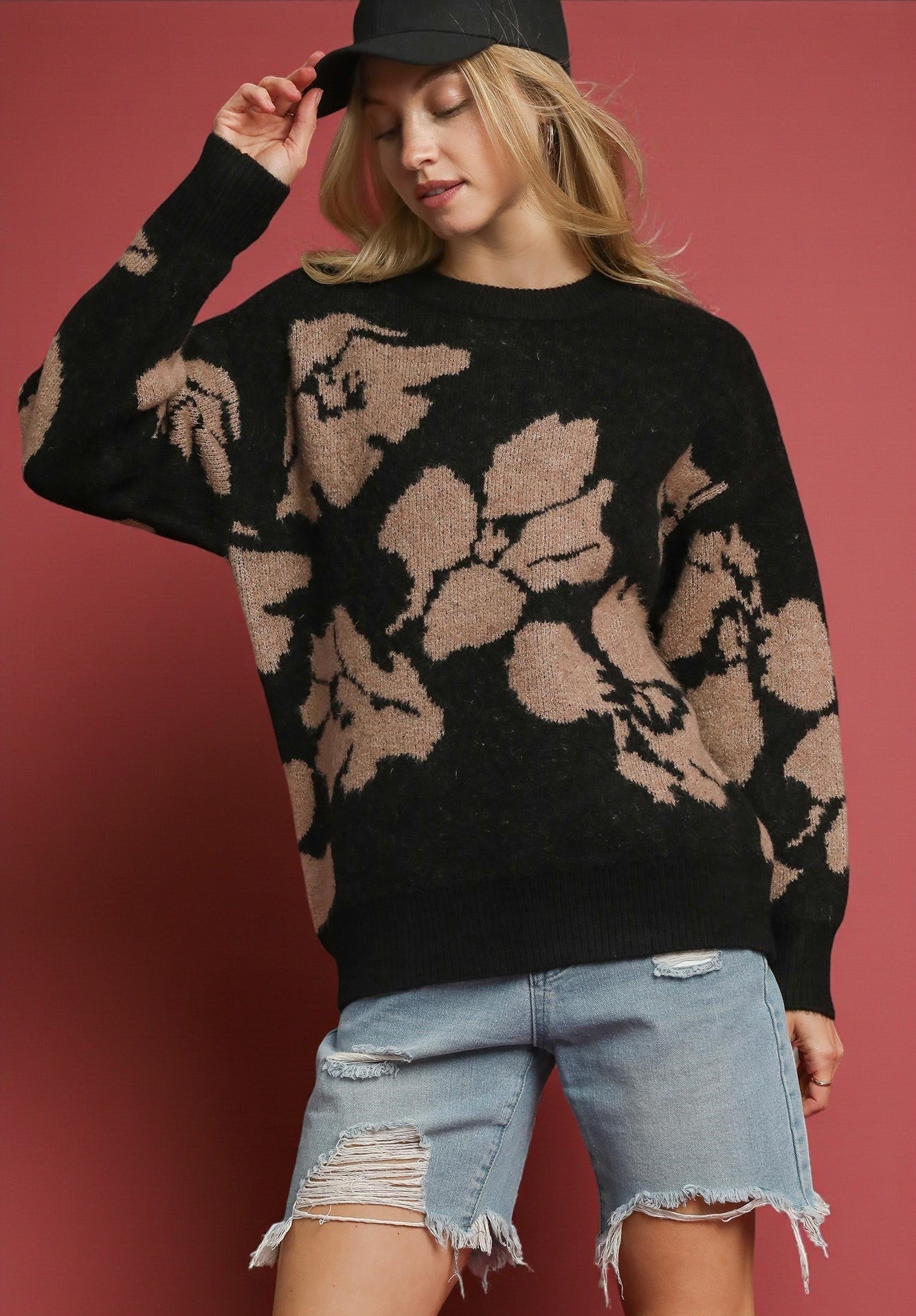 Woman wearing a black sweater with floral patterns and denim shorts against a red background