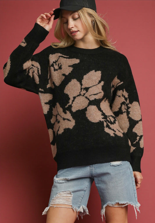 Woman wearing a black sweater with floral patterns and denim shorts against a red background