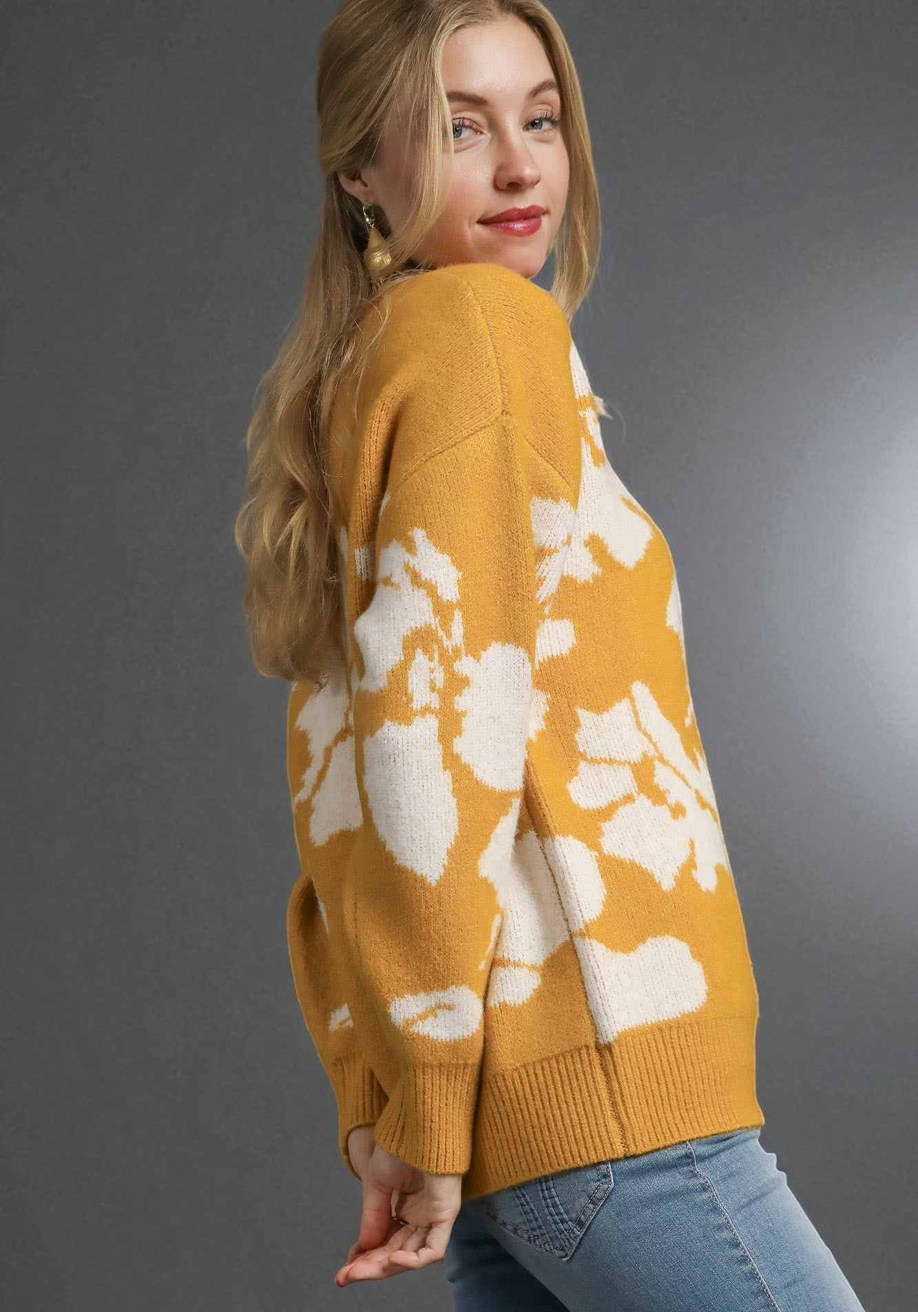 Woman wearing a mustard yellow sweater with white floral patterns on a gray background