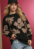 Woman wearing a black sweater with beige floral patterns against a pink background