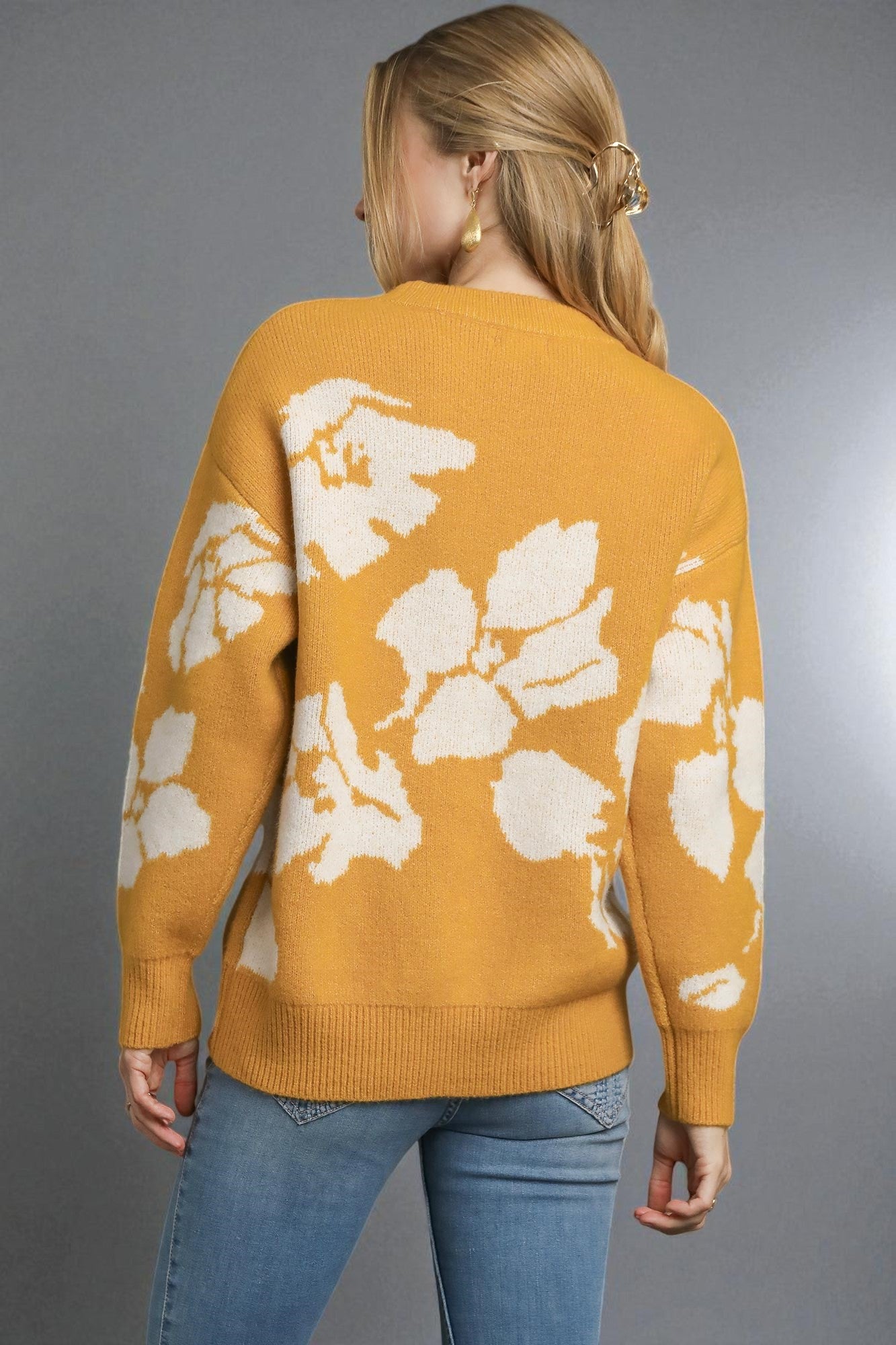 Woman wearing a mustard yellow sweater with white floral patterns on a gray background