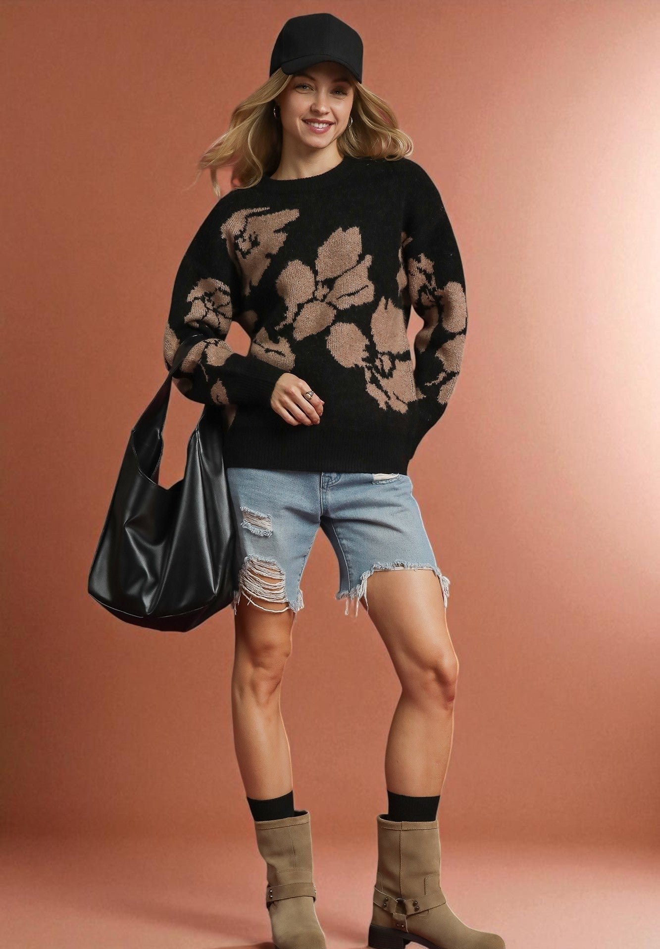 Woman wearing a black floral sweater, denim shorts, and brown boots against a pink background
