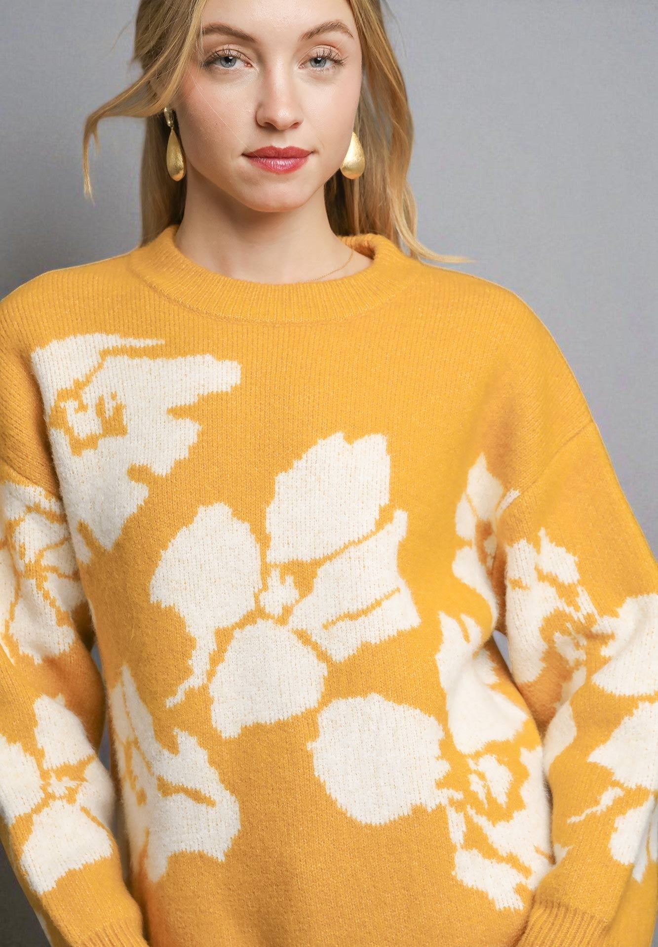 Person wearing a mustard yellow sweater with white floral patterns on a gray background