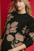 Woman wearing a black and beige floral-patterned sweater against a red background