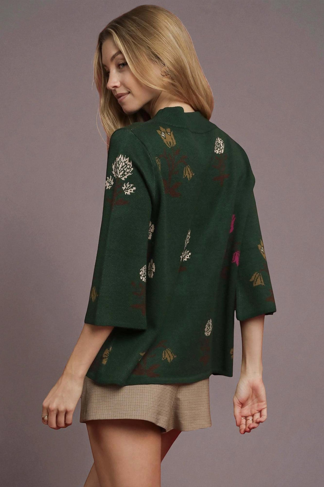 Woman wearing a dark green embroidered top against a plain background