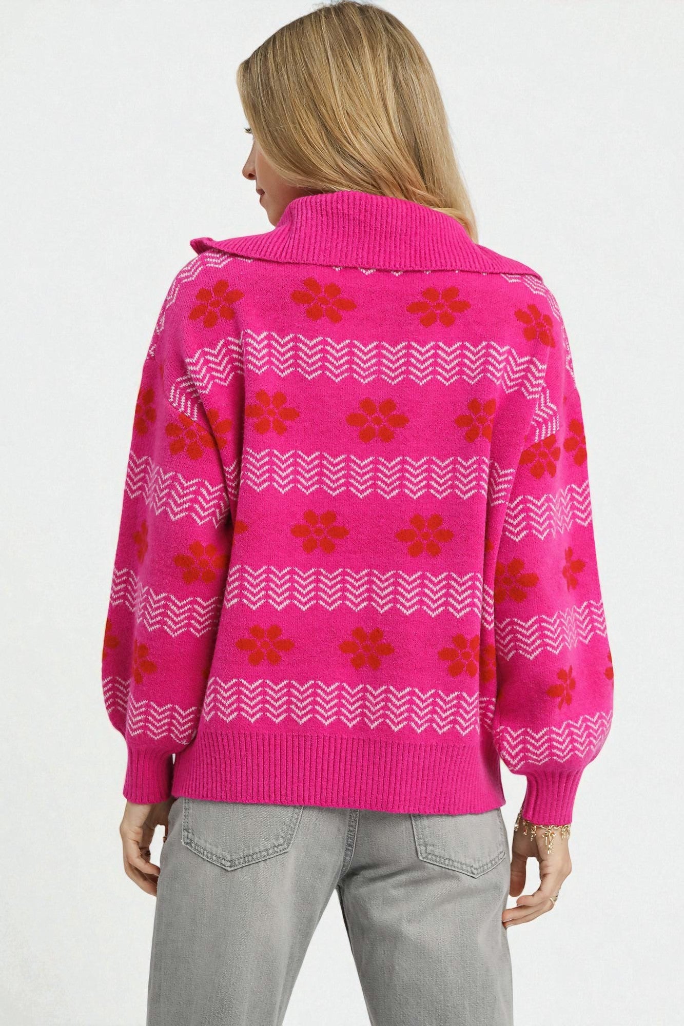 Person wearing a bright pink sweater with red floral patterns on a white background