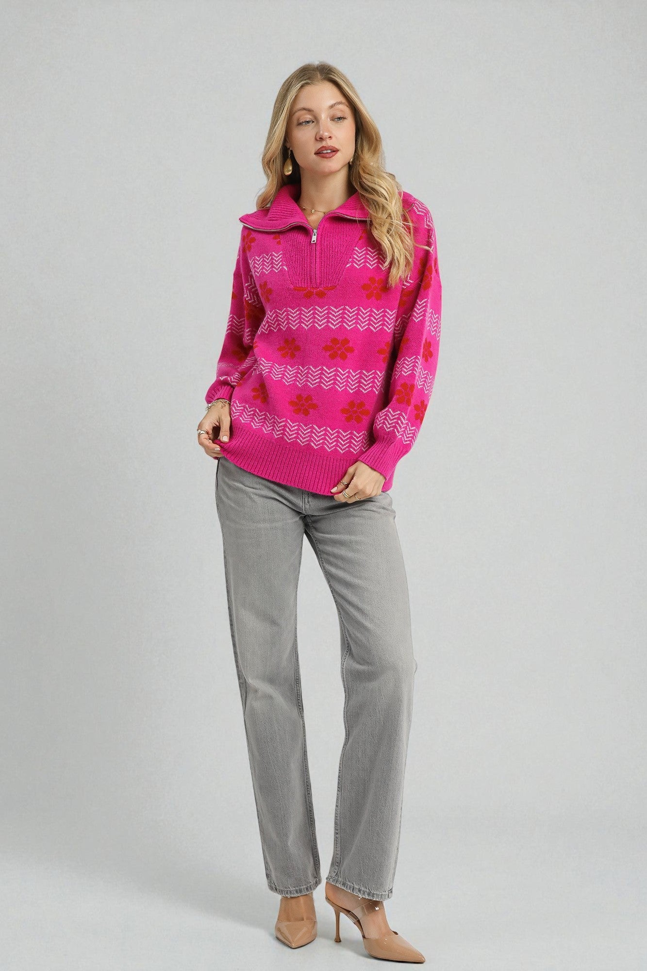 Woman wearing a pink patterned sweater and gray pants on a light gray background