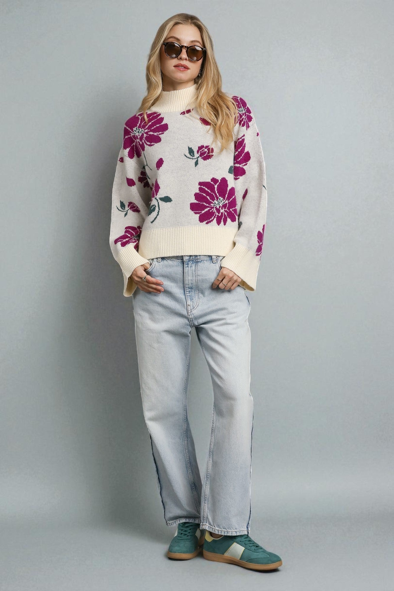 Person wearing a floral sweater, light jeans, and green shoes on a gray background