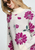 Woman wearing a cream sweater with pink floral patterns on a white background