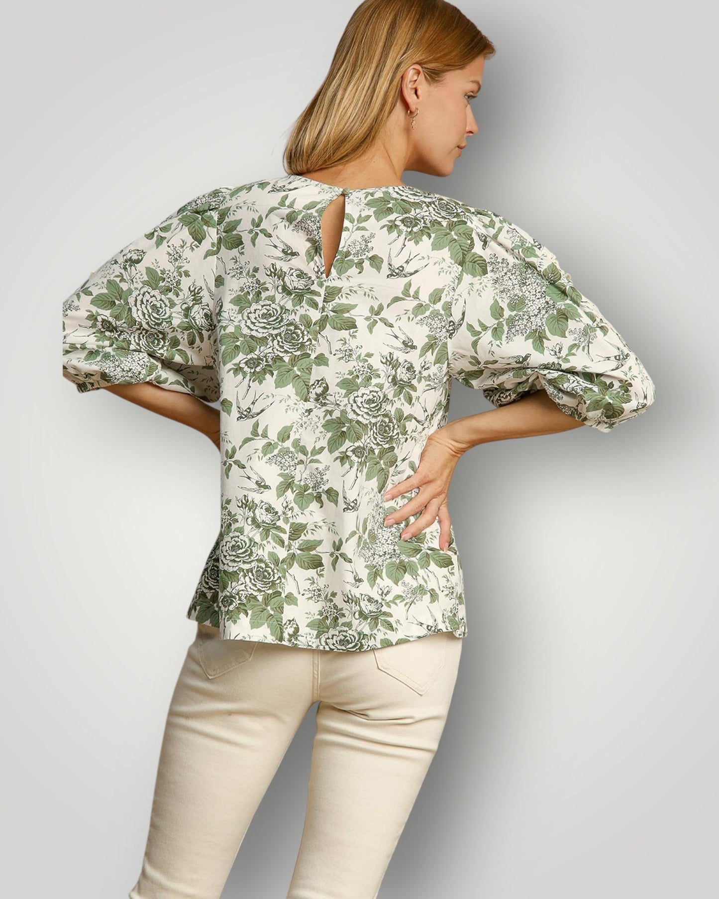 Woman wearing a green floral blouse and beige pants on a gray background