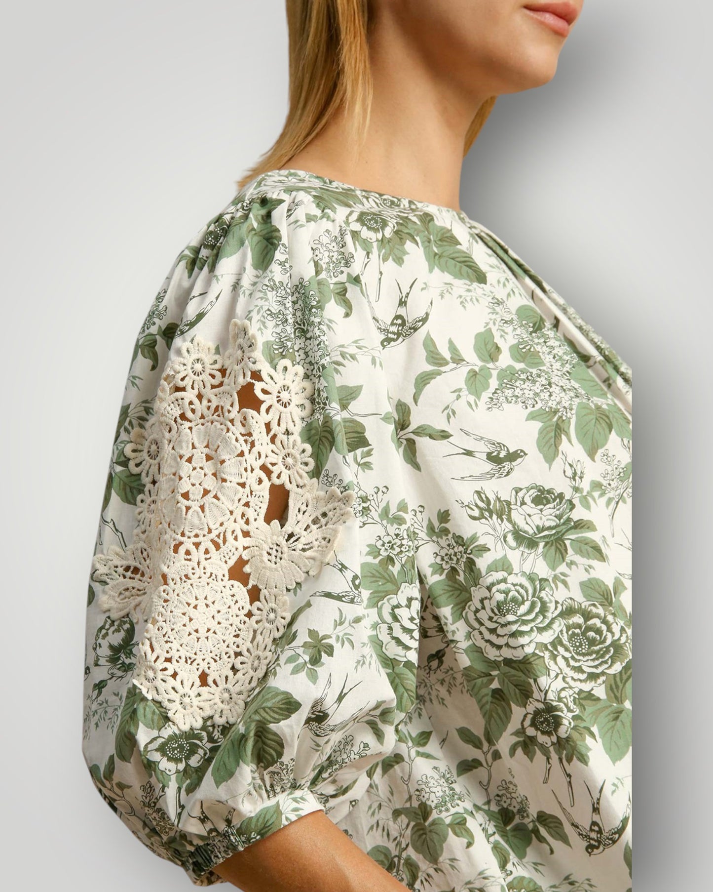 Woman wearing a floral blouse with lace details on a plain background