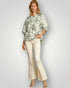 Woman wearing a floral blouse and beige pants on a plain background